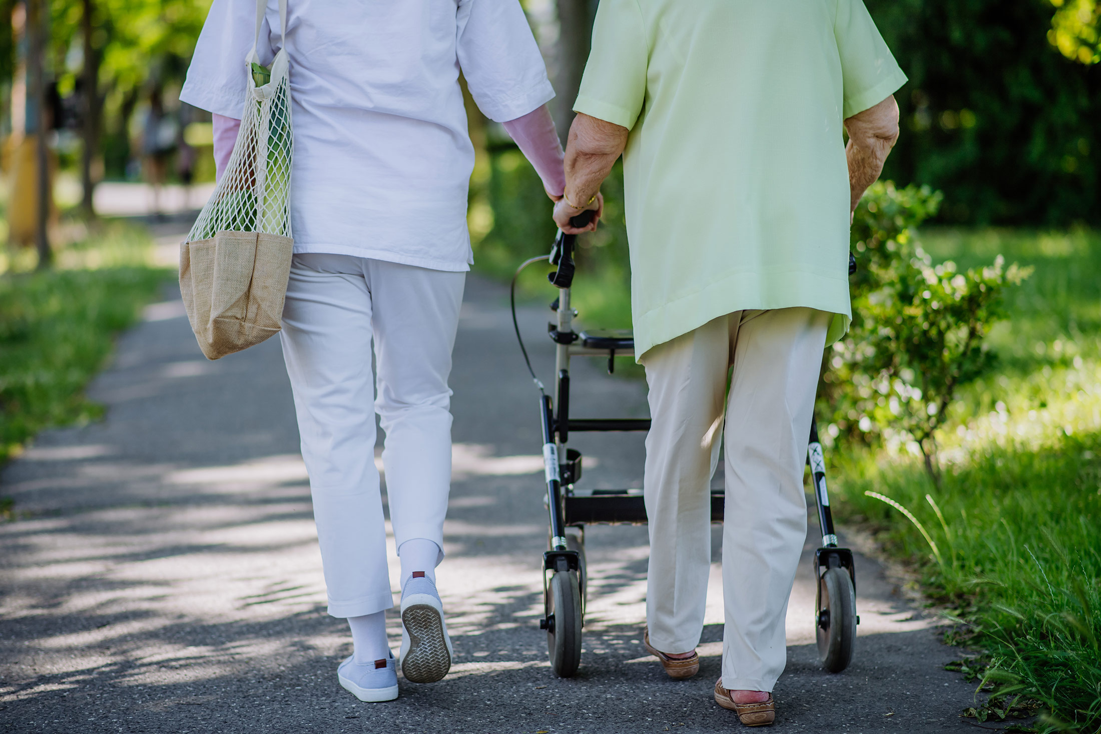 Foto von einer älteren Dame mit Rollator die mit einer Begleitung spazieren geht